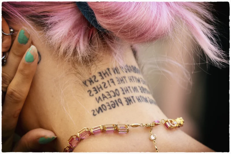 Bras avec un tatouage poétique et bracelet coloré à facettes, cheveux roses et ongles verts, fond flou
