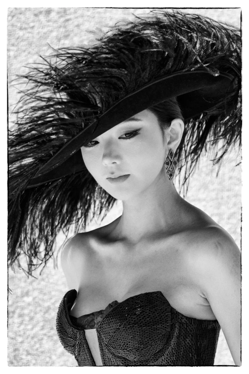 Portrait élégant d'une personne en robe moulante avec un chapeau à plumes et des boucles d’oreilles sophistiquées, en noir