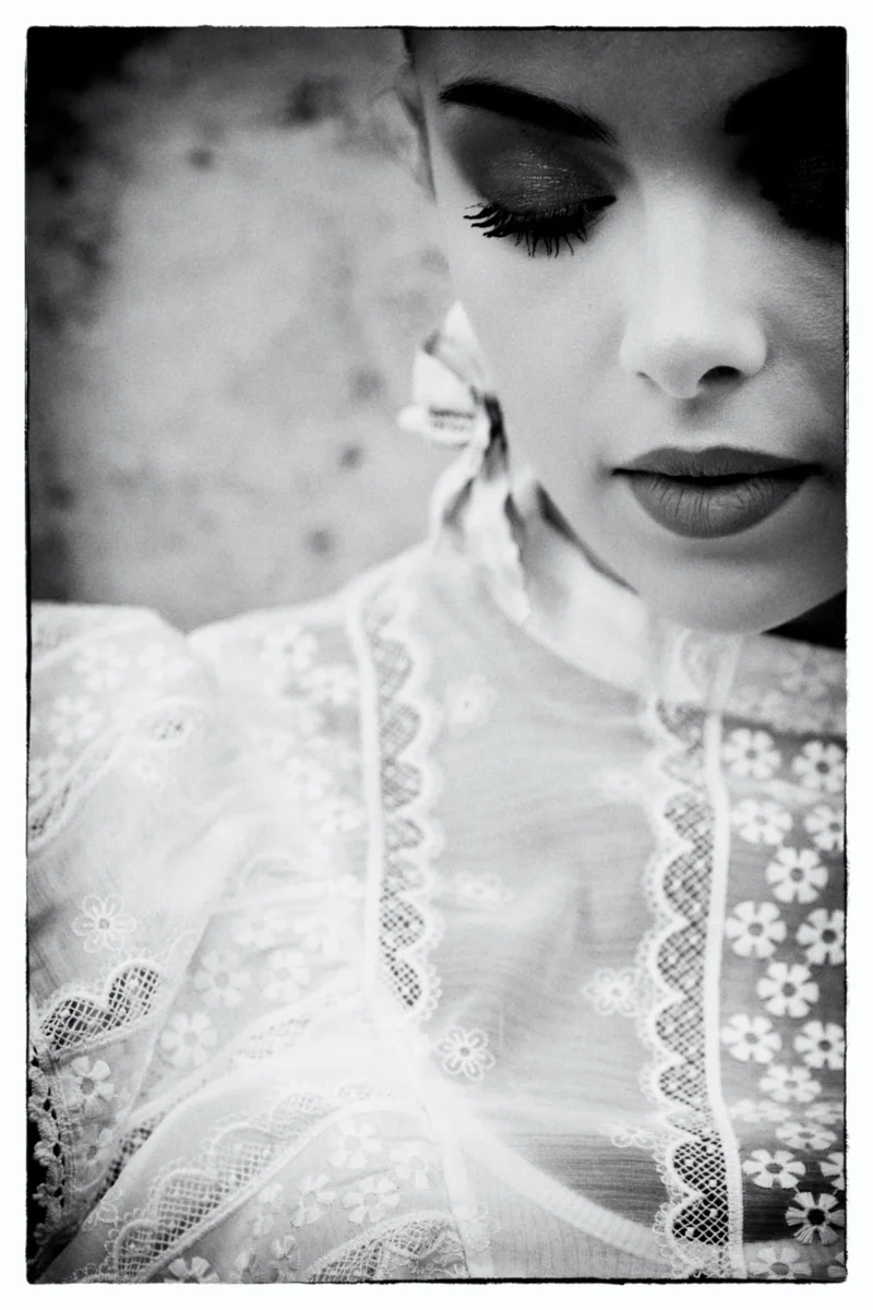 Portrait en noir et blanc d’une personne vêtue d’une robe à dentelle ajustée, regard baissé et expression contemplative
