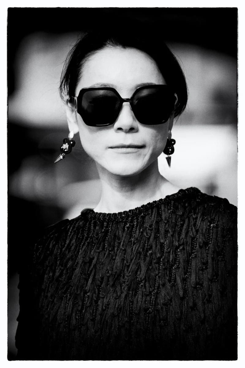 Portrait en noir et blanc d’une personne portant des lunettes de soleil et un haut texturé, expression neutre