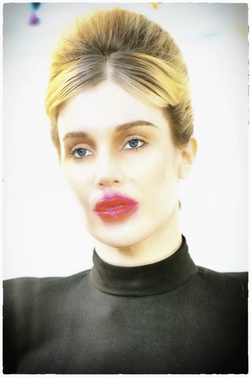 Portrait d'une personne avec une coiffure retro et un maquillage rouge à lèvres prononcé, vêtue d'un pull noir turtleneck