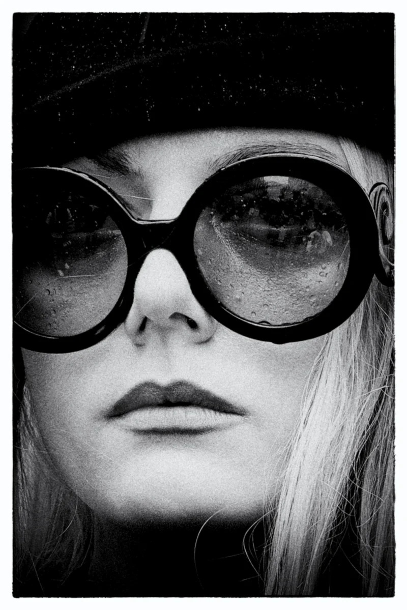 Portrait en noir et blanc d'une personne portant des lunettes à verres épais reflétant un ciel étoilé, expression neutre