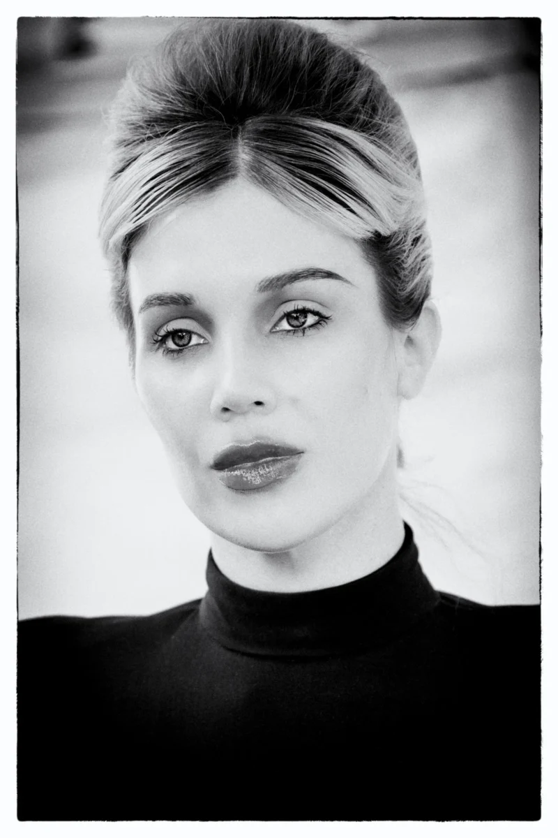 Portrait en noir et blanc d'une personne avec une coiffure retro et un t-shirt haut col, regard direct et expression neutre
