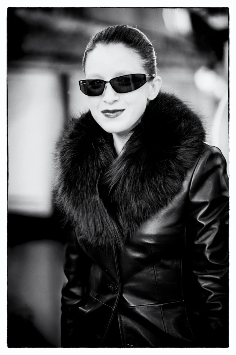 Portrait en noir et blanc d'une personne portant des lunettes de soleil et une veste en cuir à col de fourrure, ambiance