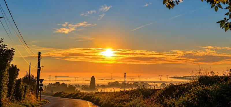 Couchant ensoleillé sur une route de campagne bordée de végétation, avec des lignes électriques et un horizon lointain