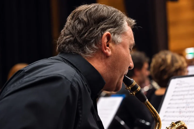 Un musicien en tenue noire joue d'un saxophone devant une partition dans un cadre concert, ambiance intimiste