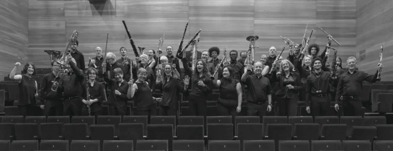 Groupe de musiciens d'orchestre assis avec leurs instruments dans une salle de concert vide, posant pour une photo