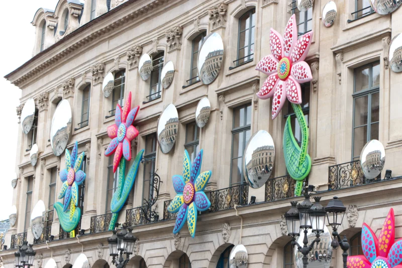 Jean paul · 29/04/2023 · 2400 x 1600 Façade d'immeuble ornée de grandes fleurs colorées en polka dots suspendues entre balcons et lampadaires, ambiance festive
