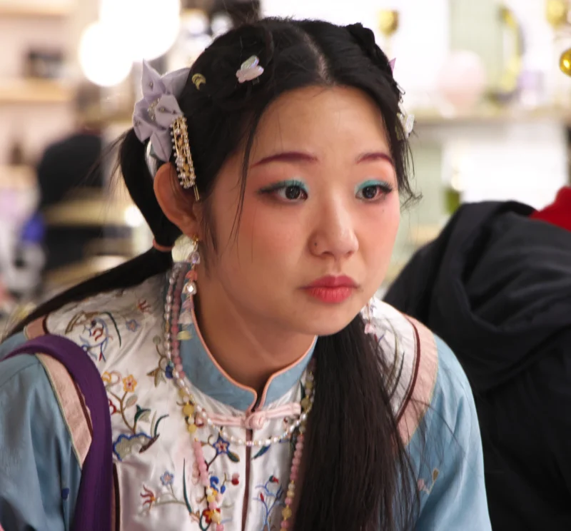 Personne vêtue d'un costume traditionnel floral aux couleurs pastel, coiffée d'un accessoire orné de fleurs, en intérieur