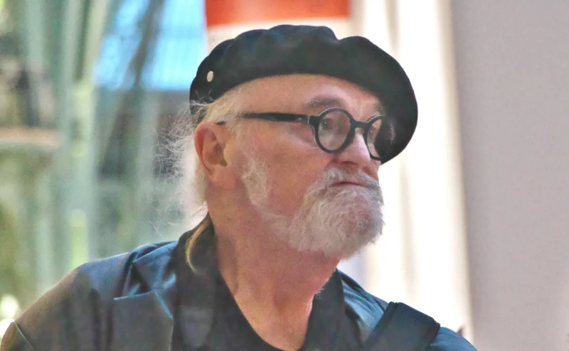 Jean paul · 14/11/2025 · 2400 x 1483 Portrait d’un homme à lunettes et chapeau noir, barbe grisonnante, en extérieur avec fond flou et lumière naturelle.