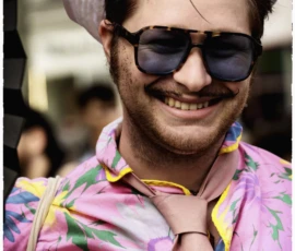 Thierry · 03/10/2026 · 1600 x 2400 Un homme souriant portant des lunettes de soleil, un chapeau et une chemise à motifs floraux, avec un badge autour du cou.
