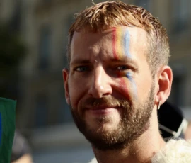 Francoise · 03/10/2026 · 2400 x 1600 Un homme souriant avec des traces de peinture arc-en-ciel sur les joues, participant à une manifestation ou célébration