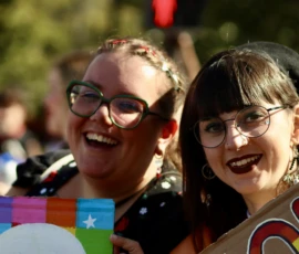 Francoise · 03/10/2026 · 2400 x 1600 Deux personnes souriantes participant à une manifestation, tenant des drapeaux aux couleurs vives et symboliques, ambiance