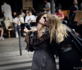 Cyrille · 03/10/2026 · 2026 x 1519 Deux personnes s'embrassent chaleureusement dans un lieu public animé, entourées de passants assis et debout