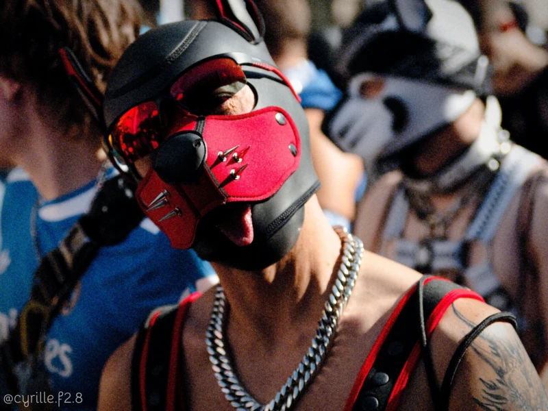 Cyrille · 03/10/2026 · 2026 x 1519 Personne portant un masque respirateur rouge et noir avec des éléments métalliques, entourée d’un collier à chaîne, dans