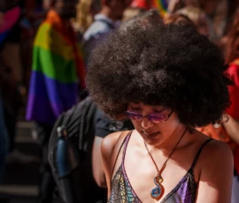 Marc · 03/10/2026 · 1080 x 1080 Personne avec une coiffure afro volumineuse portant un pendentif coloré, souriante lors d'une manifestation festive avec