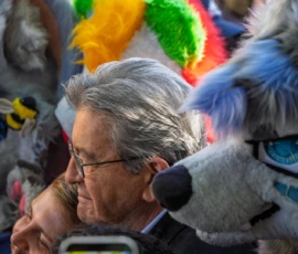 Marc · 03/10/2026 · 1620 x 1080 Un homme avec des lunettes et des cheveux gris observe un spectacle coloré avec des personnages mascottes autour de lui.