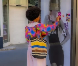 Marc · 03/10/2026 · 1080 x 1964 Une personne devant une vitrine colorée prenant une photo avec un smartphone, vêtue de couleurs vives et d'un sac