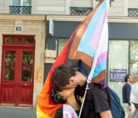 Léonard · 03/10/2026 · 1800 x 2400 Deux personnes participant à une manifestation avec des drapeaux arc-en-ciel, l'une portant un t-shirt avec un message