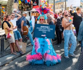 Léonard · 03/10/2026 · 2400 x 1880 Manifestant déguisé en costume coloré tenant une banderole pour la justice des migrants transgenres lors d'une marche