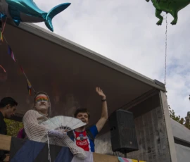 Alice · 03/10/2026 · 1920 x 2400 Deux personnes sur une scène festive avec ballons géants en forme de requin et de dinosaure, l'une agitant un éventail
