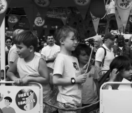 Alice · 03/10/2026 · 2400 x 1600 Enfants assis dans un véhicule festif entouré de drapeaux, participant à une fête familiale en ville, ambiance joyeuse