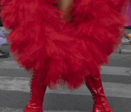 Alice · 03/10/2026 · 1920 x 2400 Personne vêtue d'une robe à volants rouges et de bottes hautes rouges, posant sur une scène ou un trottoir, style théâtral