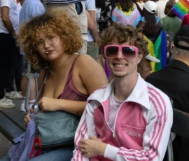 Muriel · 03/10/2026 · 2048 x 1365 Deux personnes souriantes assises lors d'un rassemblement coloré, l'une portant des lunettes roses et une veste Adidas