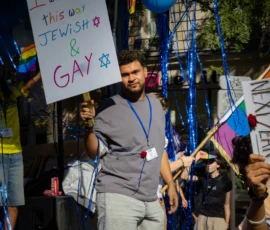 Muriel · 03/10/2026 · 2048 x 1365 Un homme participant à une manifestation avec une banderole affirmant 'this way Jewish & GAY', entouré de guirlandes et