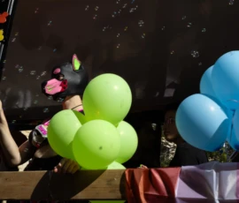 Muriel · 03/10/2026 · 2048 x 1152 Personne tenant des ballons verts dans une fête colorée avec décors et ballons bleus, ambiance joyeuse et festive sous