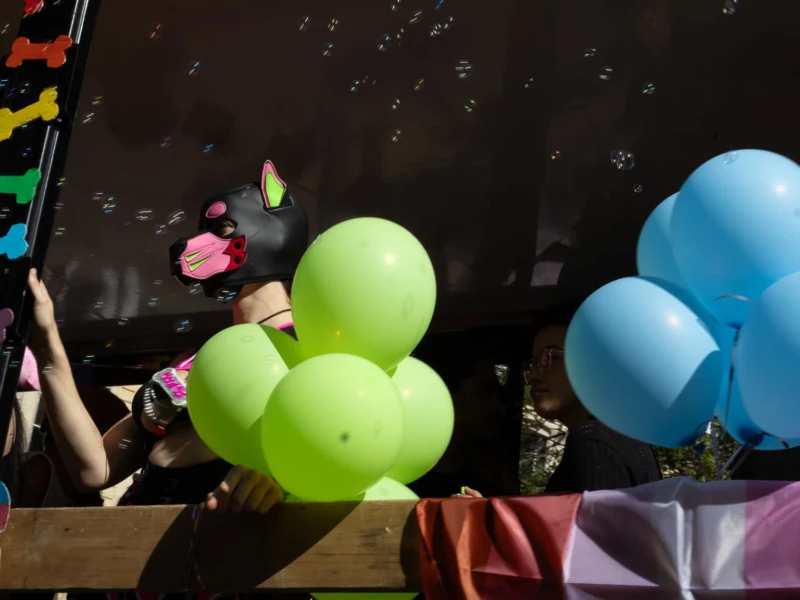 Muriel · 03/10/2026 · 2048 x 1152 Personne tenant des ballons verts dans une fête colorée avec décors et ballons bleus, ambiance joyeuse et festive sous