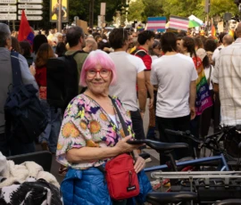 Muriel · 03/10/2026 · 2048 x 1365 Femme souriante en fauteuil roulant entouré de participants à une manifestation colorée, avec des drapeaux et des cyclistes