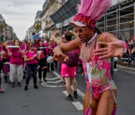 Frédéric · 03/10/2026 · 2400 x 1601 Un défilé festif avec des participants vêtus de tenues colorées, dont un personnage central en costume exubérant rose
