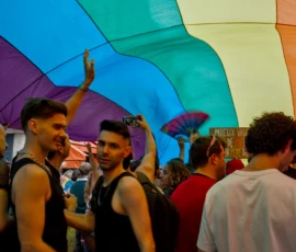 Frédéric · 03/10/2026 · 2400 x 1602 Groupe de personnes souriantes sous un drapeau arc-en-ciel lors d'une manifestation festive et colorée, ambiance joyeuse