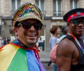 Frédéric · 03/10/2026 · 2400 x 1602 Deux personnes souriantes participant à une manifestation colorée, l'une portant un chapeau décoré et une écharpe