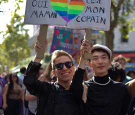 Fabienne · 03/10/2026 · 2400 x 2400 Deux personnes souriantes tenant une banderole colorée avec des messages en français lors d'une manifestation, entourées