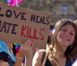 Fabienne · 03/10/2026 · 2400 x 1600 Manifestante souriante tenant une banderole avec l'inscription 'Love heals, hate kills' lors d'une marche ou rassemblement