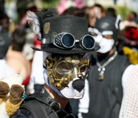 Xavier · 03/10/2026 · 2400 x 1600 Personnage déguisé en costume steampunk avec masque mécanique, chapeau à plumes et lunettes à goggles, tenant un jouet