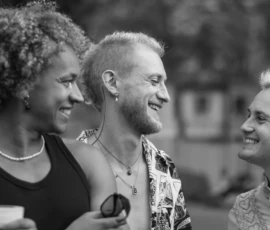 Laurence · 03/10/2026 · 1350 x 900 Trois personnes souriantes en conversation détendue, l'une tenant un objet, en extérieur avec un fond flou.