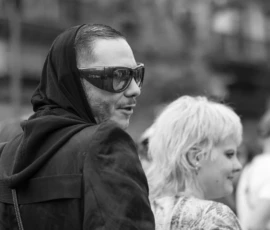 Laurence · 03/10/2026 · 1350 x 900 Portrait en noir et blanc d’une personne portant un foulard et des lunettes de soleil dans un environnement urbain animé