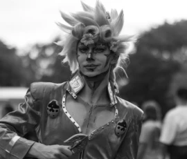 Laurence · 03/10/2026 · 1350 x 900 Personnage déguisé en costume futuriste avec coiffure extravagante et maquillage stylisé, posant devant un public flou