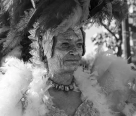 Laurence · 03/10/2026 · 1350 x 900 Personne vêtue d'un costume festif traditionnel couvert de plumes et de paillettes, sourire joyeux, participant à