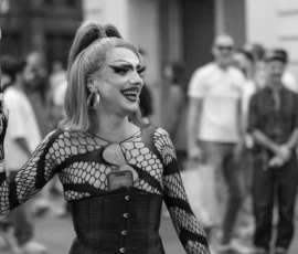 Laurence · 03/10/2026 · 1350 x 900 Personne en tenue futuriste et corset élancé, riant en marchant en ville avec un accessoire à la main et un téléphone à